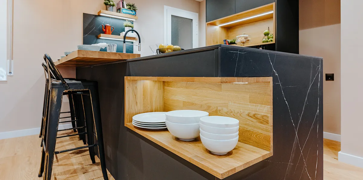 Cocina con isla en negro y nicho de madera iluminado