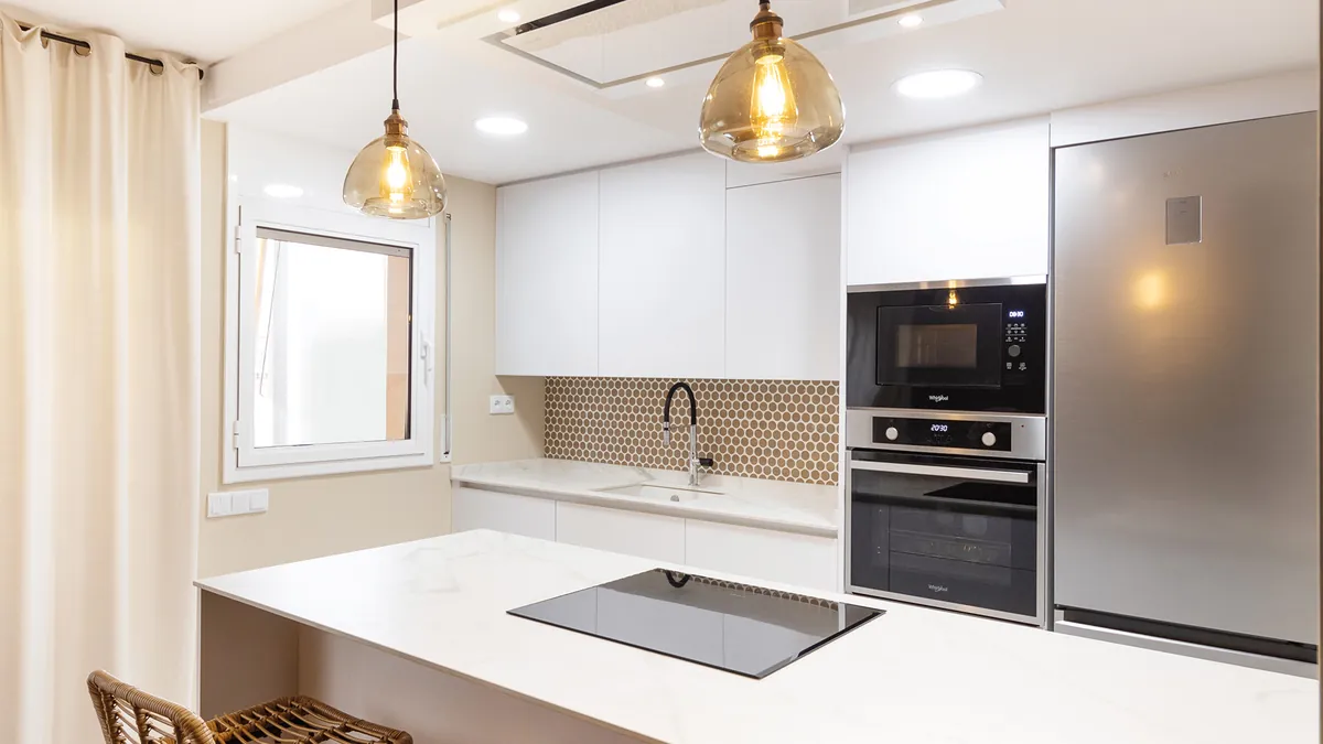 Cocina blanca con revestimiento de mosaico y lámparas doradas